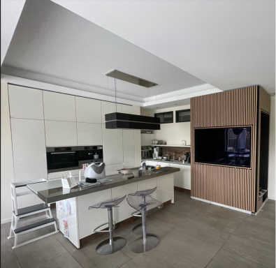 Moderne Küche mit hellen Oberflächen, Barhockern und einem großen Fernseher.