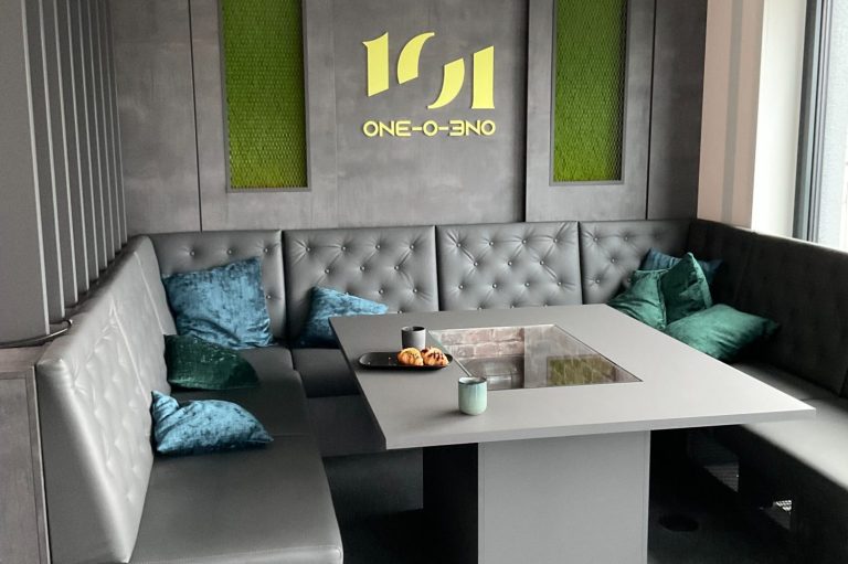 Moderne Lounge mit grauem Tisch, gepolsterten Sitzbänken und dekorativen Kissen.